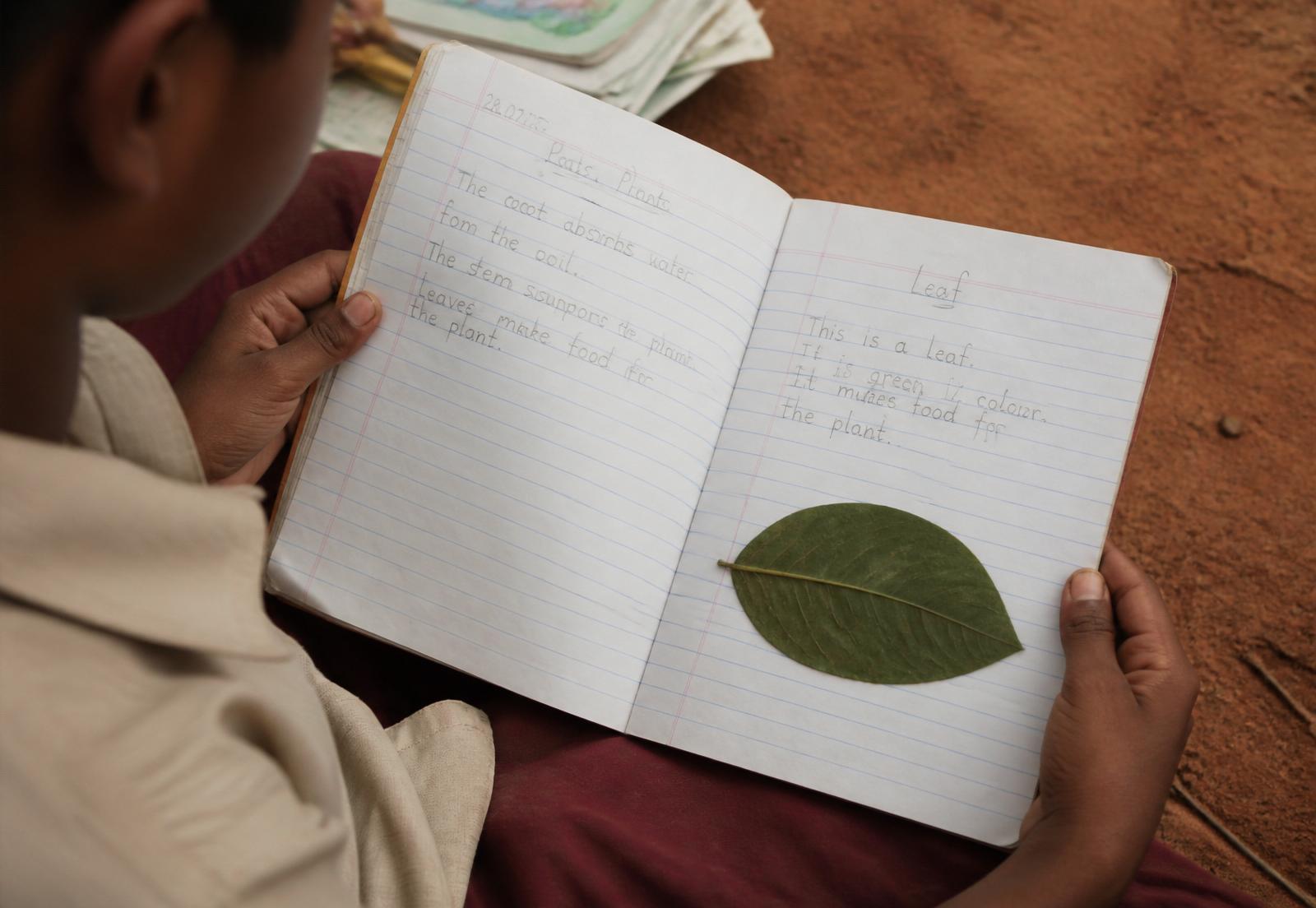 A child's handwritten notebook with a pressed leaf