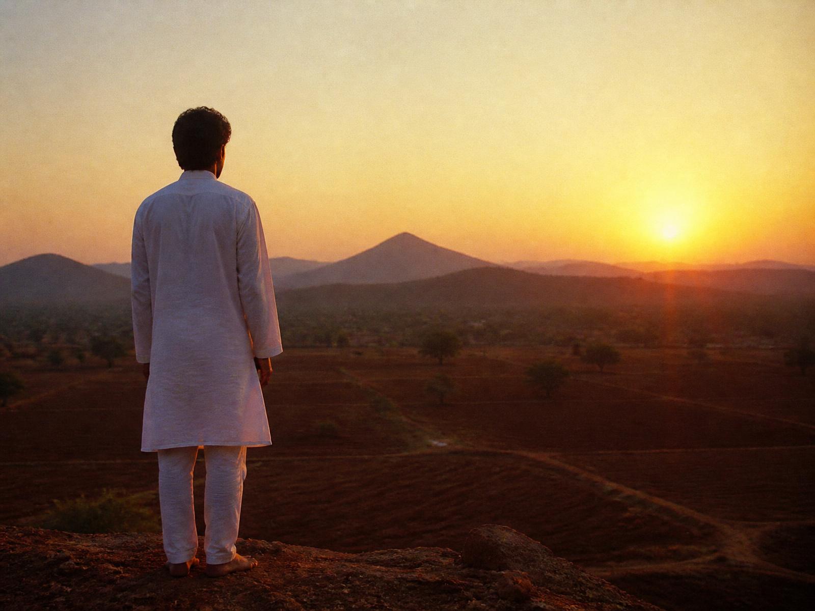 A figure in white kurta looking out over the red-earth land at sunrise